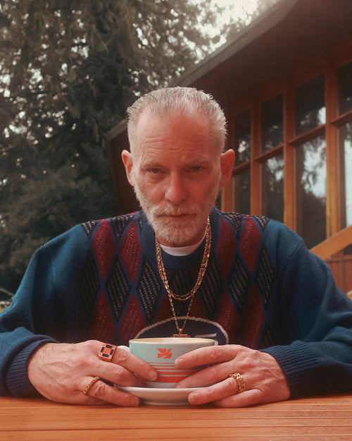 FW24 Editorial man sitting with his hands around a latte wearing MAPLE 14K Gold rings chains and necklaces