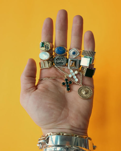 Palm of hand infront of yellow background wearing multiple MAPLE Rings and holding Necklaces