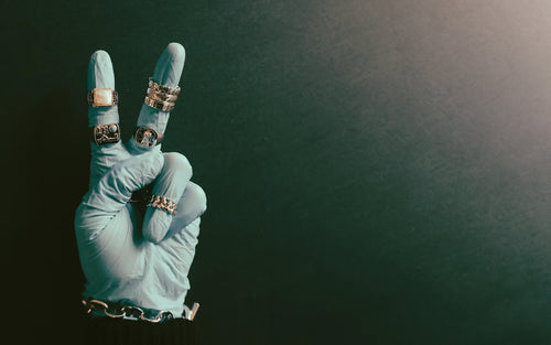Palm facing hand making peace sign wearing blue surgical glove and MAPLE rings & bracelets