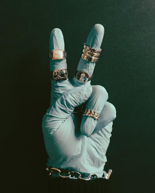 Palm facing hand making peace sign wearing blue surgical glove and MAPLE rings & bracelets