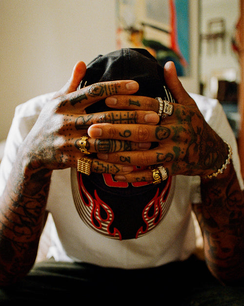 Man head down wearing cap with tattooed hands clasped around the top of his head