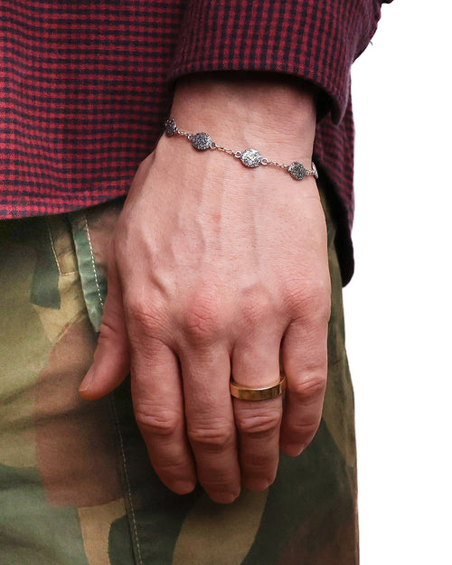 Hand wearing a bracelet and ring with a checkered shirt and green pants.