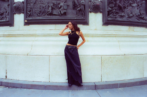 Anissa standing on a curb against a white marble wall with Parisian wall sculpted art