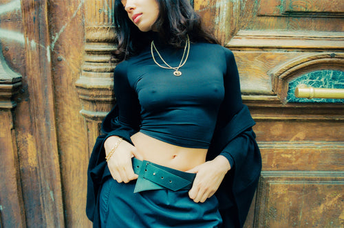 Anissa leaning against an old wooden door with thumbs tucked into belt wearing MAPLE 14K Gold jewelry