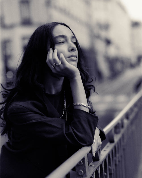 Anissa with her elbow on a bridge railing and hand under chin looking into the distance showing off MAPLE jewelry