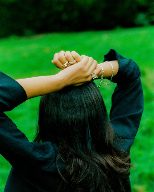 Top back angle view of Anissa with hands atop her head wearing MAPLE rings & bracelets