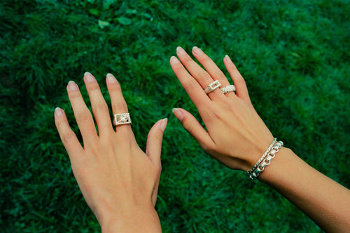 Woman's hands above grass wearing and showing off MAPLE bracelets & rings