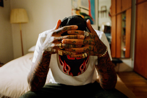 Artist Chino Creese sitting on his bed with head looking down and hands clasped on top of his head