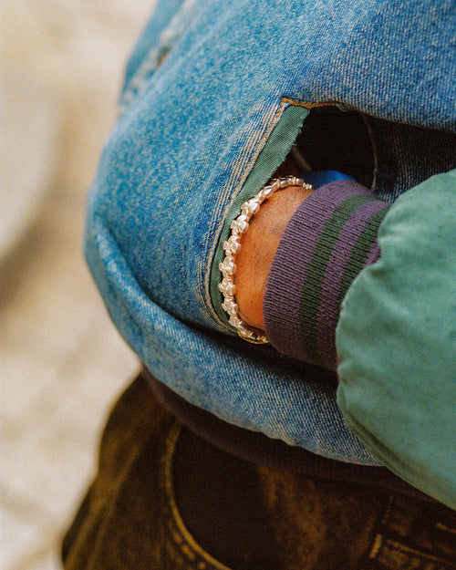 Hand in pocket of 90s denim jacket with MAPLE Cross bangle peaking out