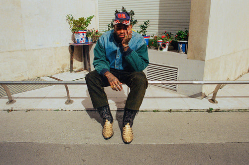 Artist Chino Creese sitting on low metal railing with hand resting on chin and face