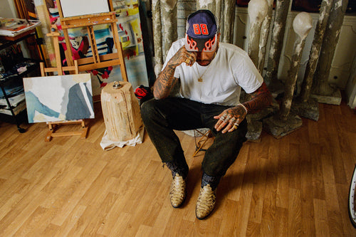 Artist Chino Creese sitting in front of his art & sculpture in his studio