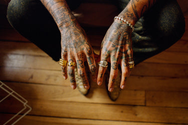 Artist Chino Creese sitting with arms resting on knees showing off MAPLE rings and bangle